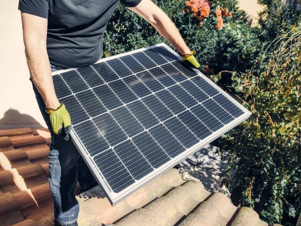 A Person in Black Shirt Holding a Solar Panel while Standing on the Roof